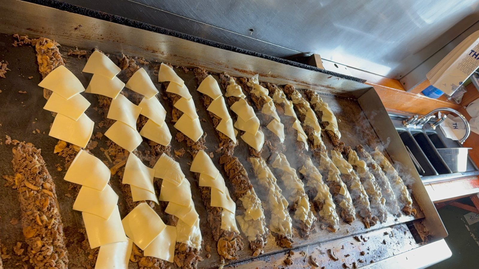 Rows of chopped Calozzi's steak topped with melting white cheese on the flat-top grill